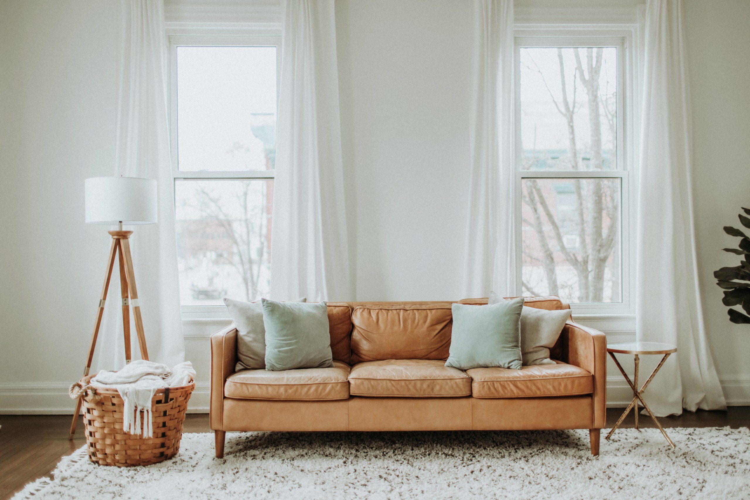 Imagem de uma sala decorada com luminária, sofá na cor mostarda e um tapete neutro felpudo.