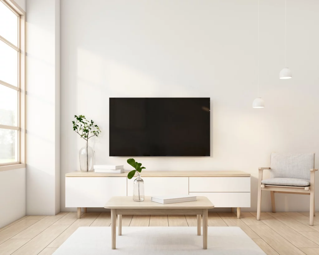 Imagem da decoração de uma sala e estar com um rack minimalista, mesa de centro e televisão pendurada na parede