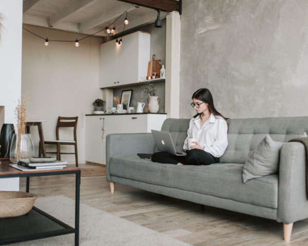 Foto de uma sala de estar moderna em tons de cinza e elementos em madeira. Na foto há uma mulher sentada no sofá cinza, há também um tapete e uma mesa de centro.