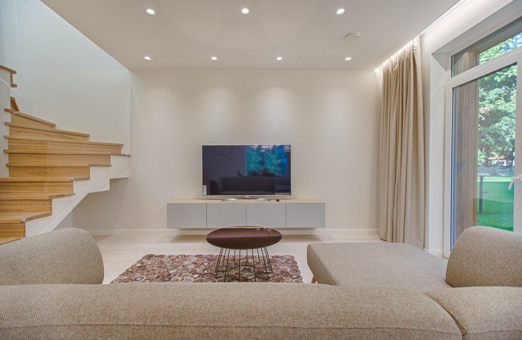 Foto de uma sala de estar moderna em tons de bege. Na foto há um sofá grande, um tapete, uma mesa de centro, um hack e uma TV.