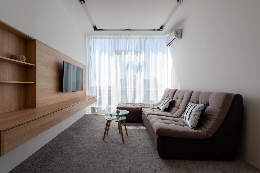 Foto de uma sala de estar moderna com um sofá bem confortável, um conjunto de 2 mesinhas de centro e um hack acoplado à parede com TV.