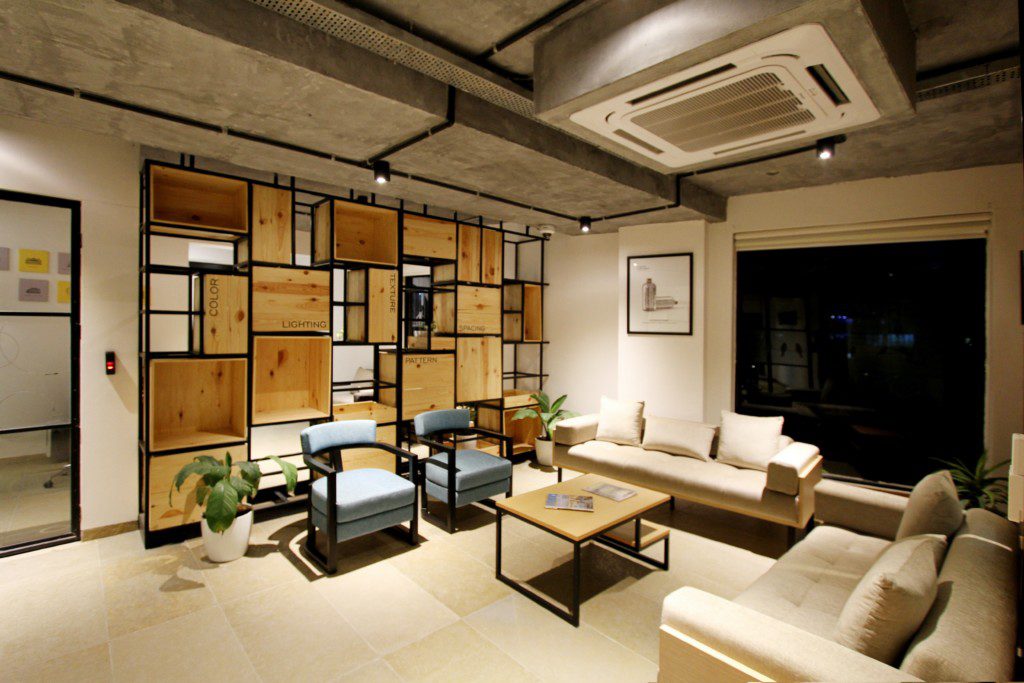 Foto de uma sala de estar moderna ampla com diferentes elementos. Destaque para uma estante em metal com prateleiras em madeira, dois sofás confortáveis, duas poltronas estilosas e uma mesa de centro. 