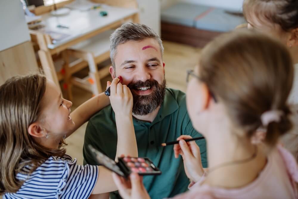 Foto que ilustra matéria sobre decoração para dia dos pais mostra duas meninas brincando de maquiar o pai.