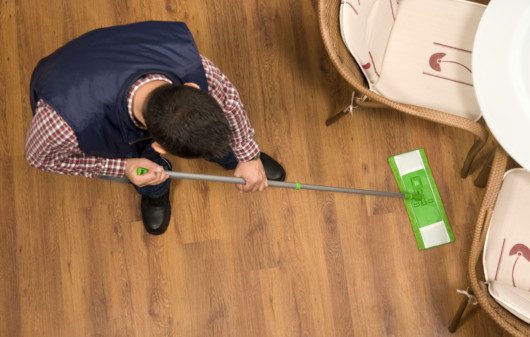 Imagem de um homem limpando um piso laminado com estilo amadeirado.