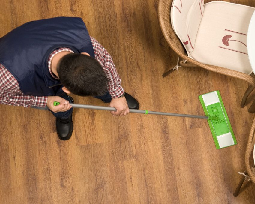 Imagem de um homem limpando um piso laminado com estilo amadeirado.