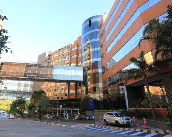 Foto que ilustra matéria sobre hospitais em São Paulo mostra a fachada do Hospital Israelita Albert Einstein, localizado no Morumbi. Um prédio com janelas espelhadas do meio para o canto direito da imagem e com uma passarela fechada por vidros, que liga o mesmo prédio a outro, que não aparece na imagem.