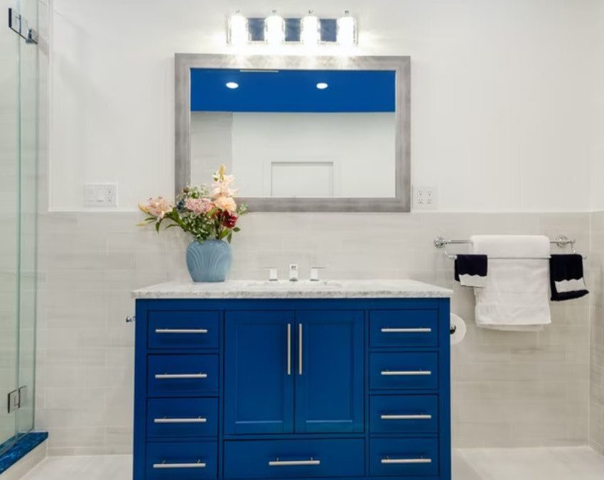 uma das ideias de armário para banheiro, esse em tom azul vivo, contrastando com o branco do ambiente