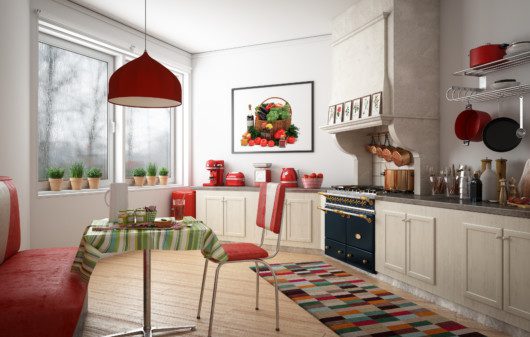 A foto mostra um exemplo de cozinha retrô em tons de vermelho e bege. Há um armário com puxadores redondos e uma bancada com os utensílios à mostra. Tem também uma mesa com banco.