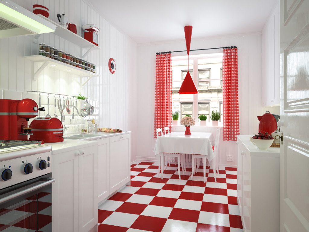 A foto mostra um exemplo de cozinha retrô com piso xadrez vermelho e branco. A cozinha está completa com fogão, cafeteira, torradeira, armários em toda ela e também outros itens.