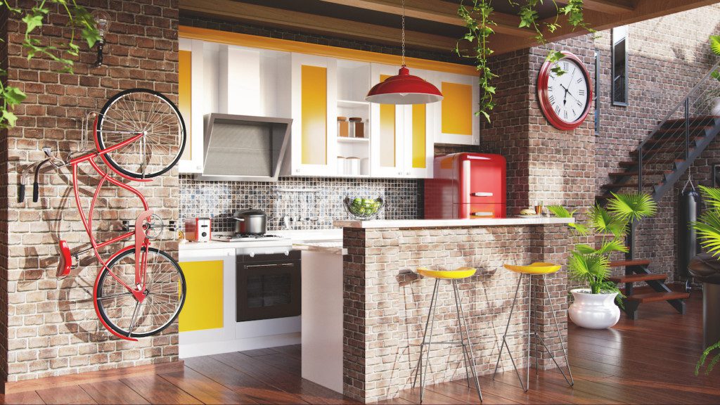 A imagem mostra uma cozinha tipo americana com uma bancada, estantes embutidas na parede com tons amarelo e branco, elementos em vermelho (uma bicicleta pendurada na parede, a geladeira, um lustre de teto e o relógio de parede), além de utensílios como fogão, coifa, panela, entre outros.