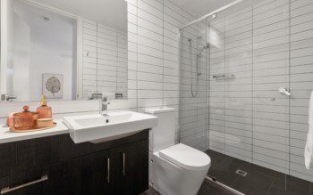 Banheiro com revestimento de cerâmica na cor branca e armário marrom