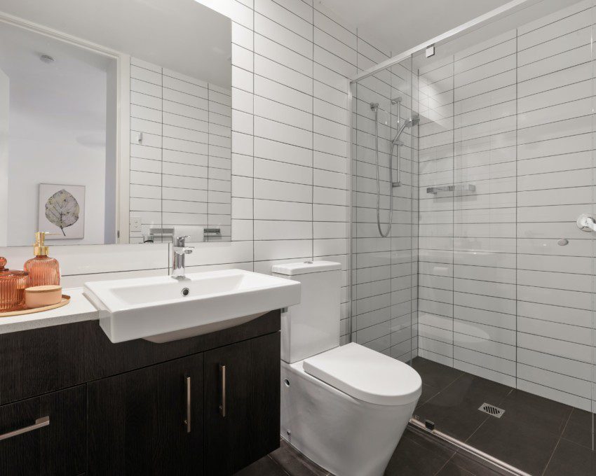 Banheiro com revestimento de cerâmica na cor branca e armário marrom