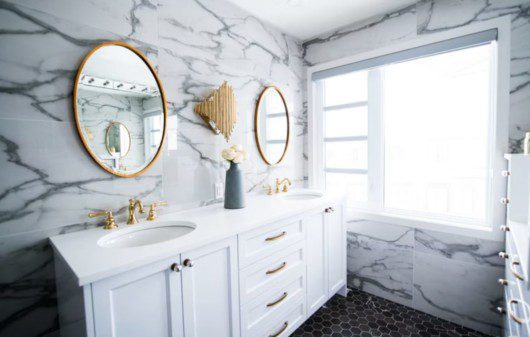 banheiro moderno com paredes de mármoer, espelhos redondos e móveis claros