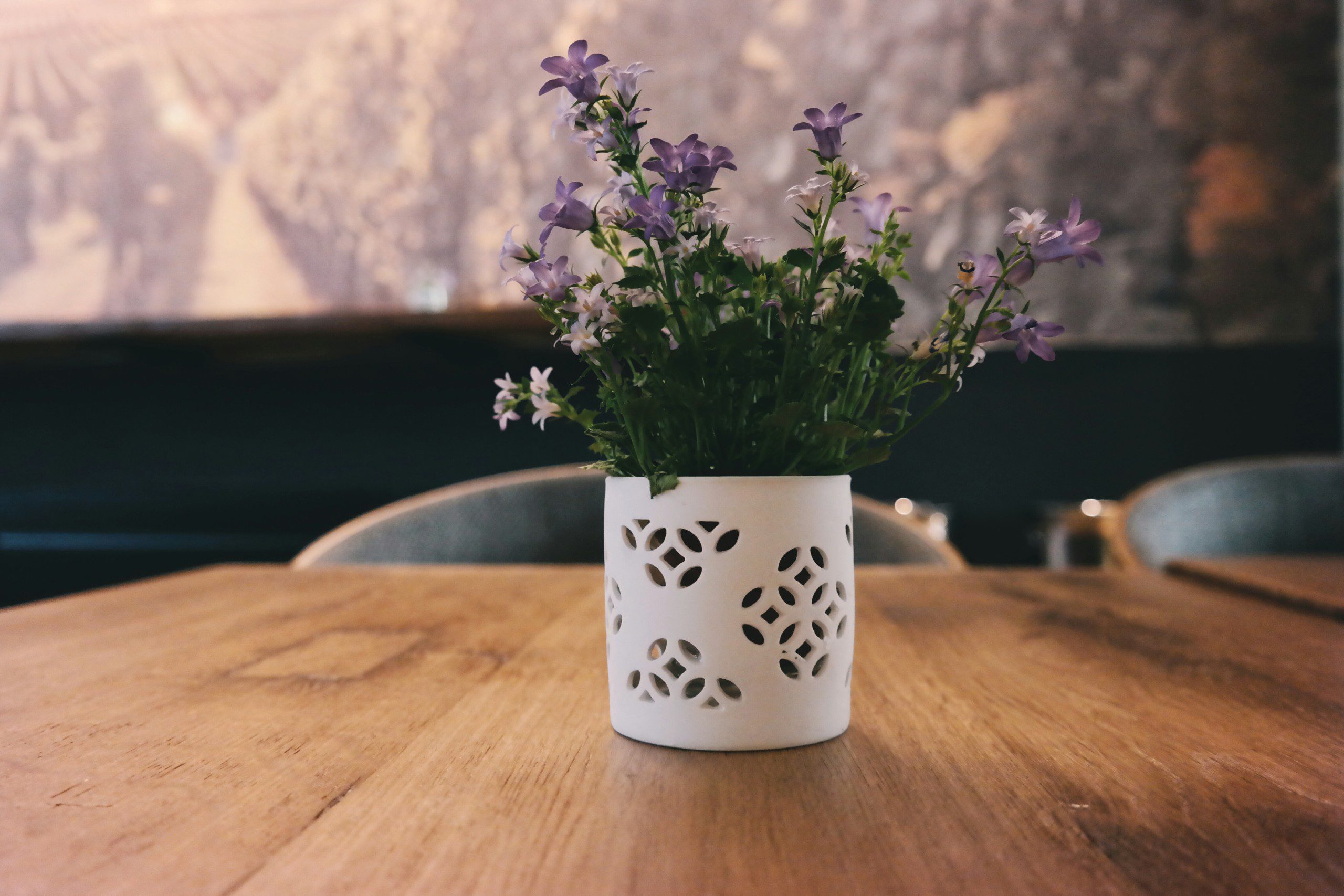 Imagem de um vaso de flor branco com flores artificiais estilo violeta.