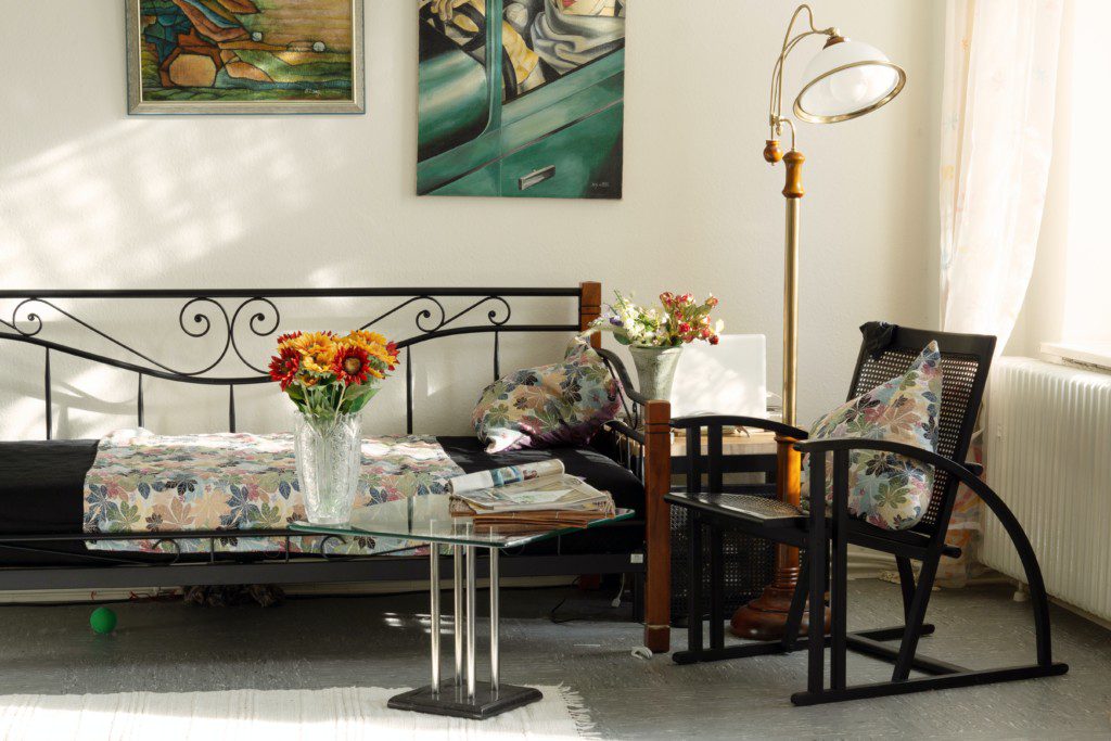 Imagem de uma sala de estar com poltrona, sofá, tapete e uma mesa de centro com um vaso de flores artificiais. 