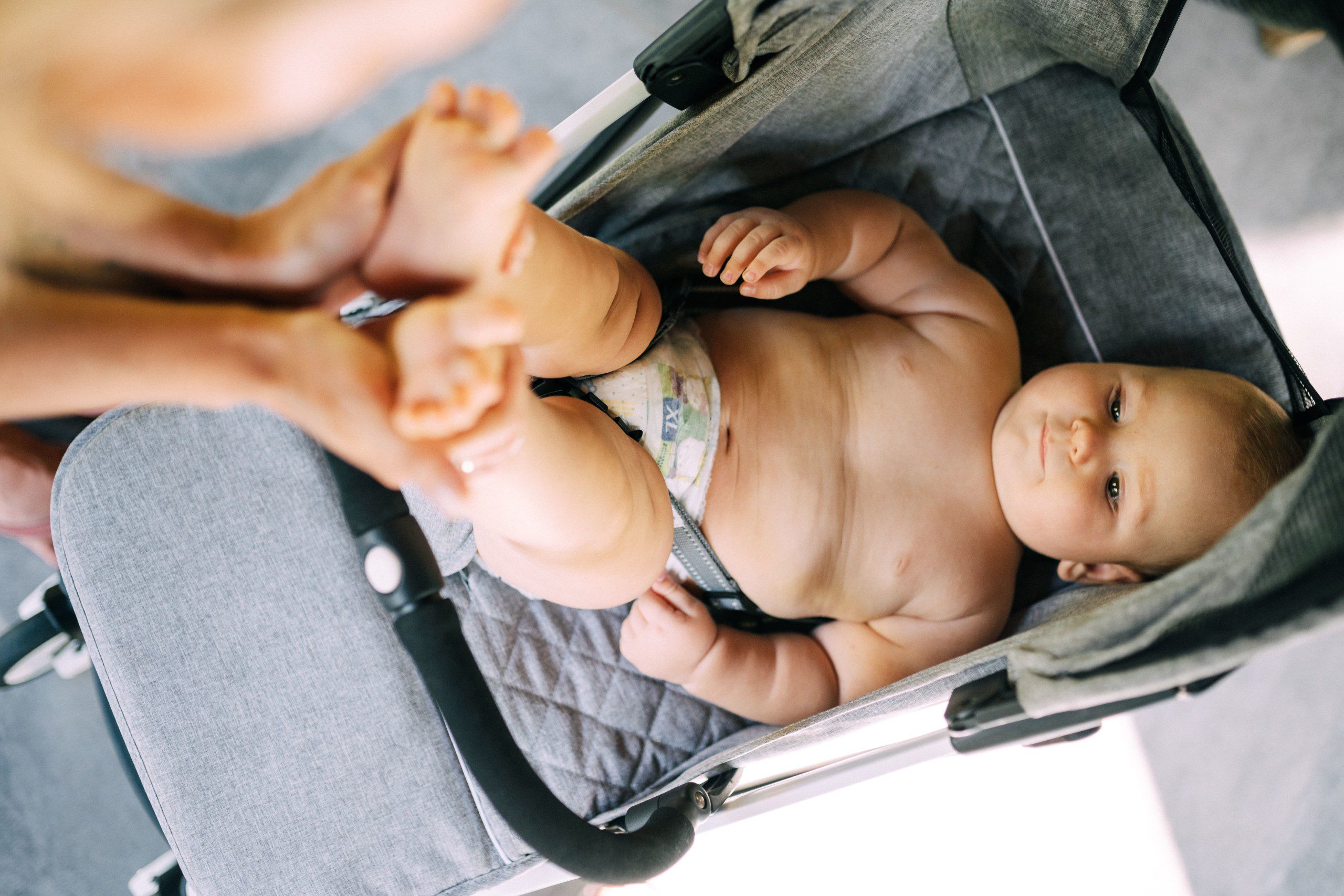 Imagem de uma bebê só de fraldas em um carrinho de bebê.