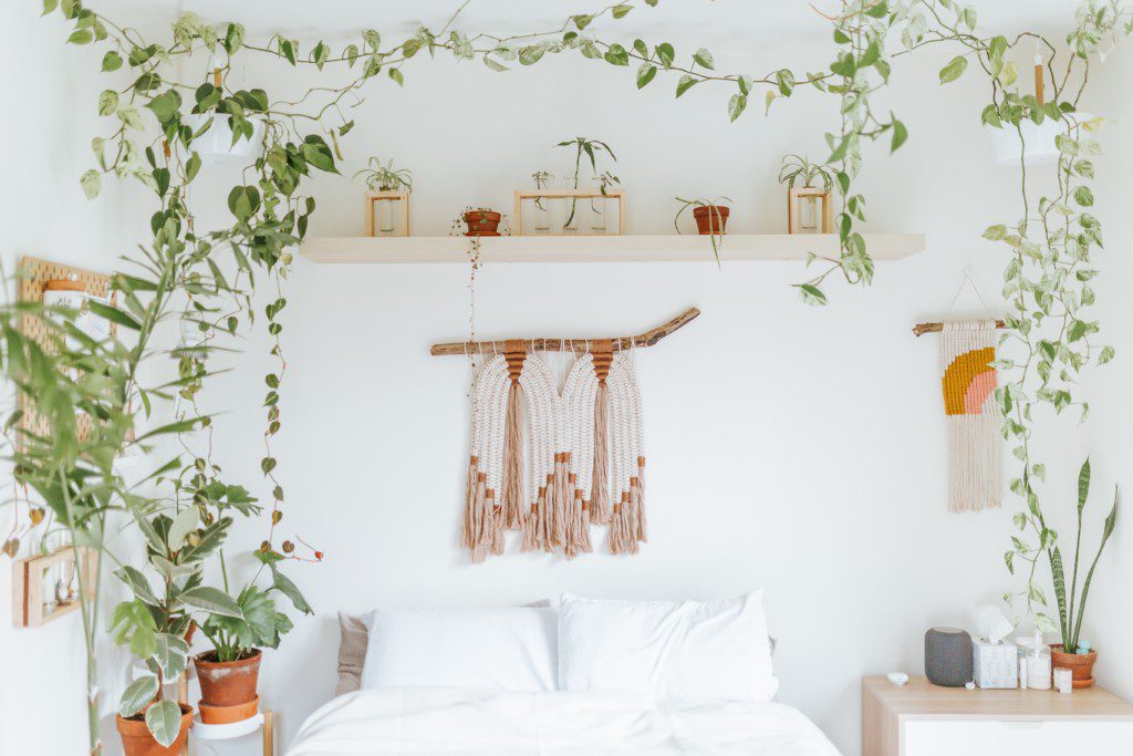 Foto de quarto casal boho composto por cama, plantas e muitos itens de artesanato.