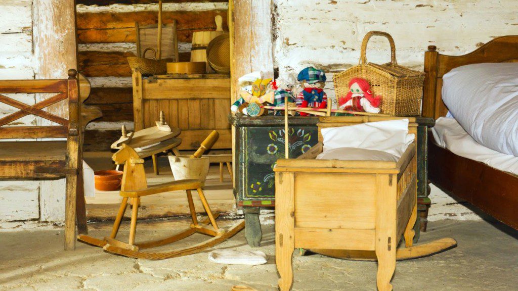 quarto infantil com berço,cavalinho de brinquedo, armários e itens de madeira e parede de tijolos
