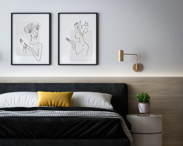 quarto com decoração minimalista. Cama com coberta preta e almofadas amarelas, quadros acima da cama com desenhos e pequena mesa com planta