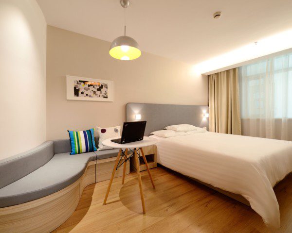 Foto de um quarto moderno com cama, sofá e mesa de apoio. O sofá acompanha a curva que a parede faz.