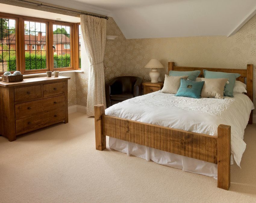 quarto rústico com cama de casal, janela lateral iluminando a cômoda de madeira, e mesas de cabeceira também de madeira