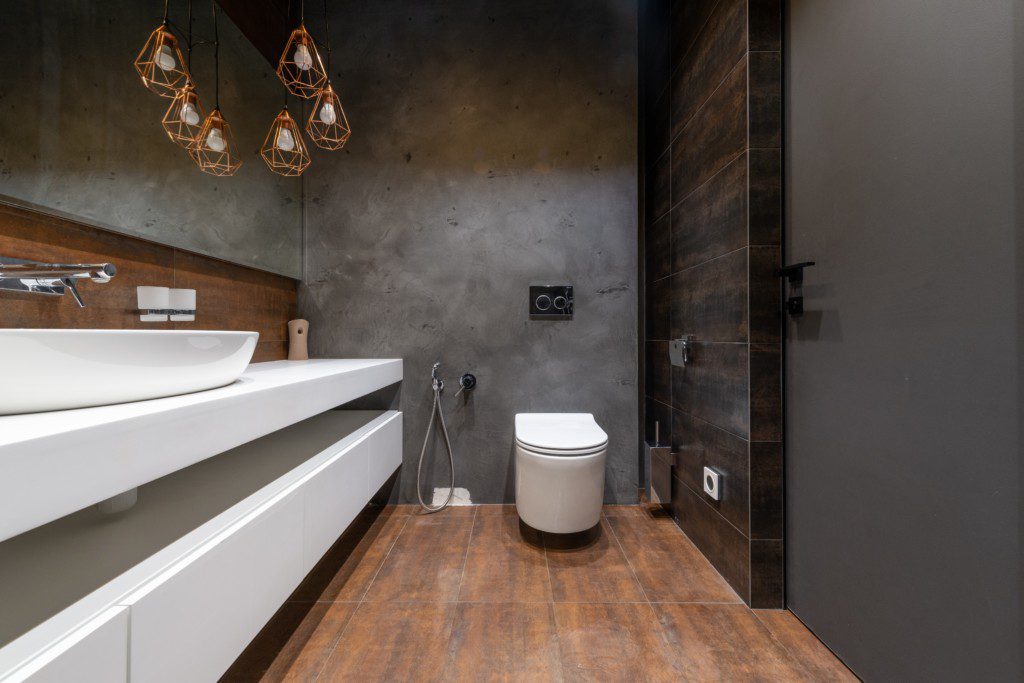  Imagem de um banheiro moderno com parede de cimento queimado e móveis brancos.