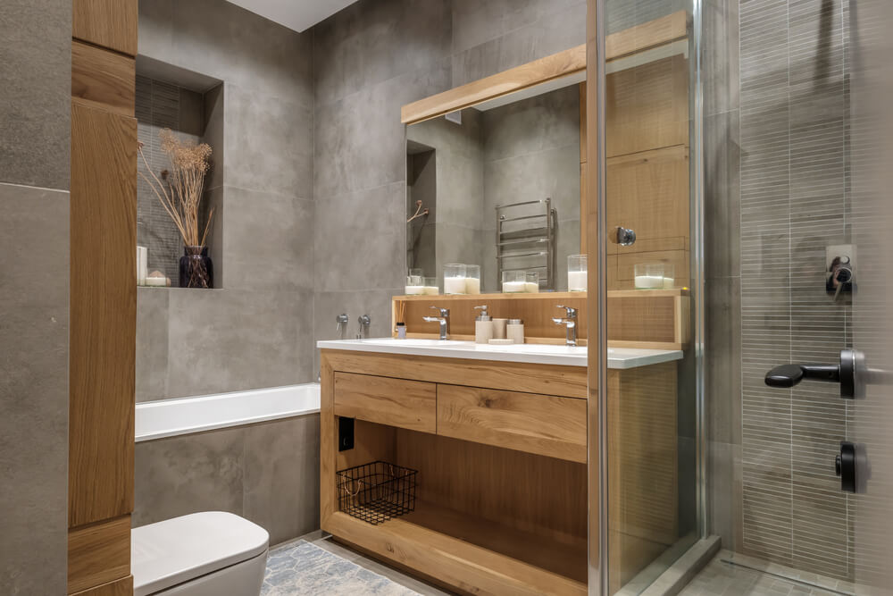 Foto que ilustra matéria sobre banheiro planejado mostra um banheiro pequeno, com um armário feiito sob medida de madeira, um box de vidro à direita, uma banheira no canto esquerdo e um vaso sanitário.