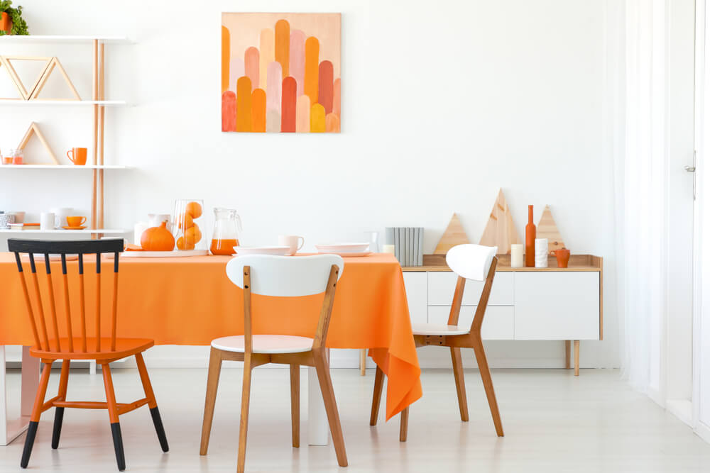 Foto de uma sala de jantar com tons de laranja na mesa, no quadro e nas decorações.