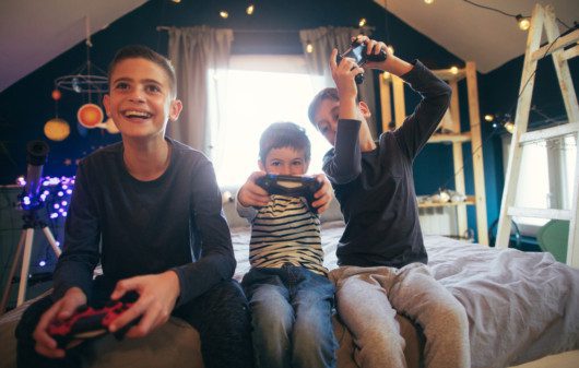 Imagem que ilustra matéria sobre quarto para 3 filhos mostra 3 crianças jogando videogame
