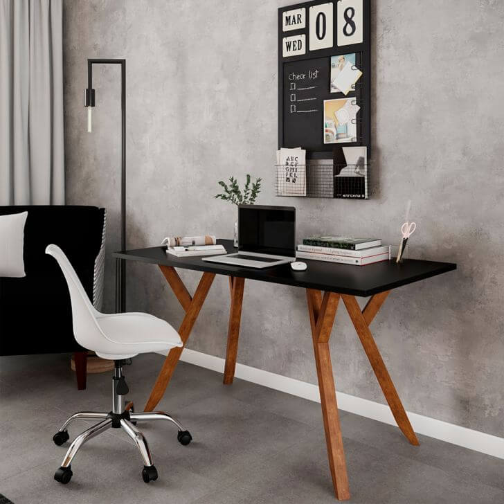 Foto que ilustra matéria sobre decoração de escritório moderno mostra uma mesa de trabalho com tampo preto e pés de madeira, encostada em uma parede cinza, junto com uma cadeira branca de rodinhas. 