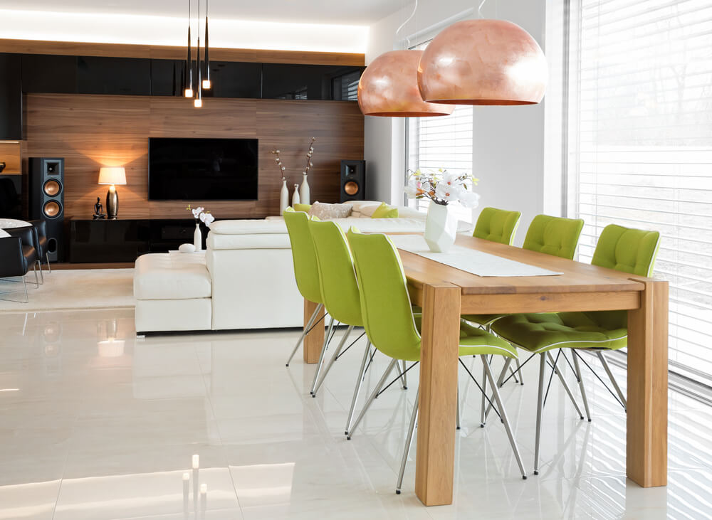 Foto que ilustra matéria sobre decoração de mesa mostra uma mesa de jantar com seis lugares integrada a uma sala de estar com uma televisão ao fundo e um sofá de costas para a mesa.