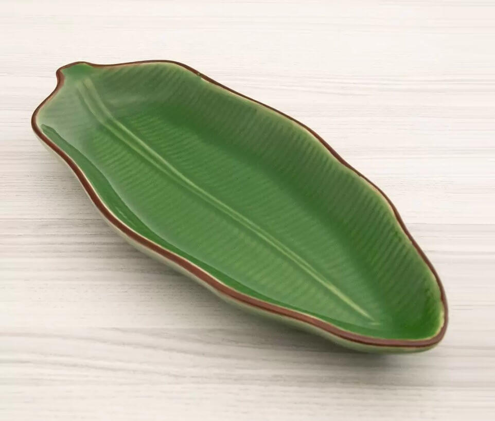 Foto que ilustra matéria sobre decoração de mesa mostra um centro de mesa de cerâmica verde em forma de folha.