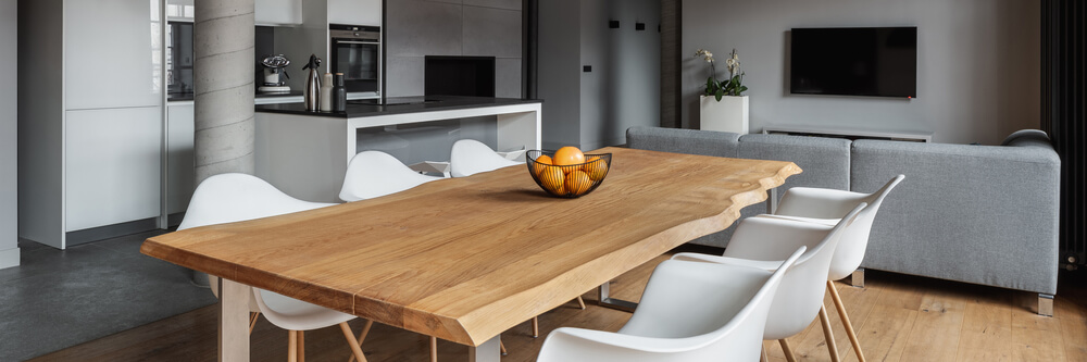Foto que ilustra matéria sobre decoração de mesa mostra uma mesa de jantar com seis lugares e com uma cesta de frutas cheia de laranjas. A sala de jantar é integrada com a de estar e a cozinha