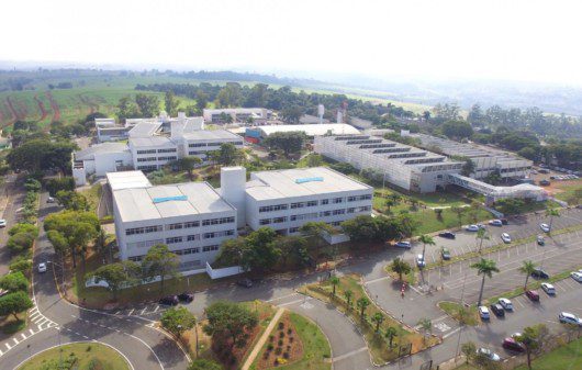 Foto que ilustra matéria sobre Faculdades em Campinas mostra uma visão aérea do Campus I da PUC-Campinas, um conjunto de prédios cercados por áreas de estacionamentos e áreas gramadas.