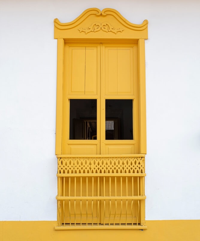 Foto que ilustra matéria sobre frente de casa simples mostra uma janela amarela se destaca nessa parede de duas cores, onde o branco predomina com uma faixa no mesmo tom de amarelo na parte inferior.
