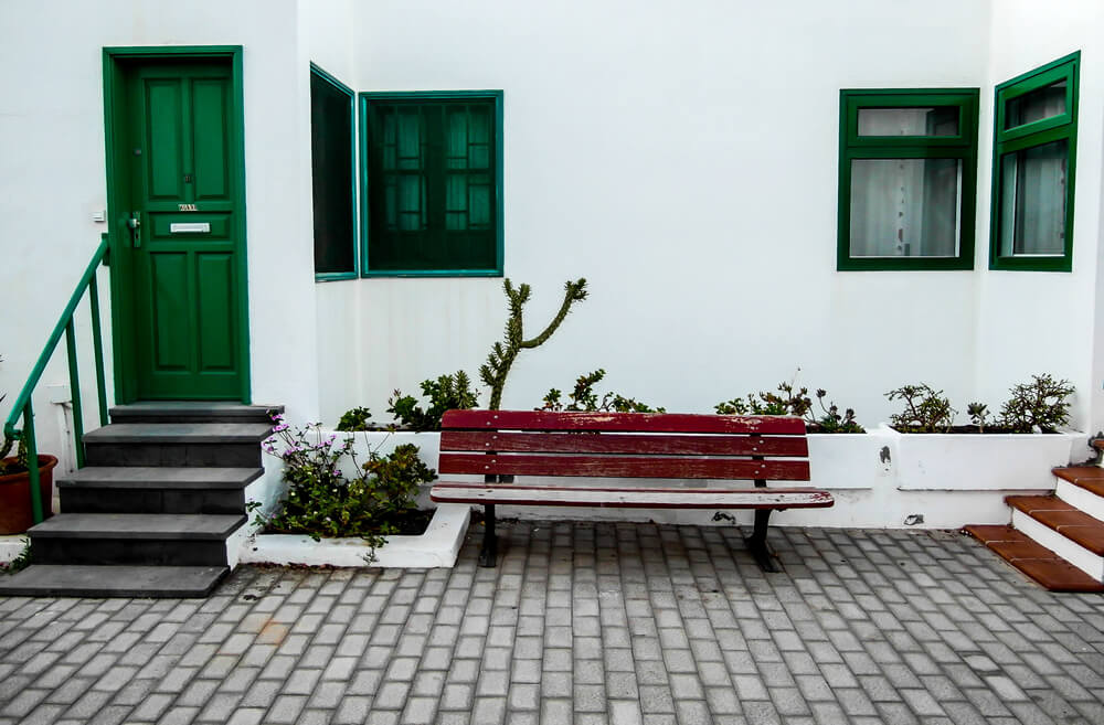 Foto que ilustra matéria sobre frente de casa simples mostra uma casa branca, em que as janelas e a porta verde saltam aos olhos.