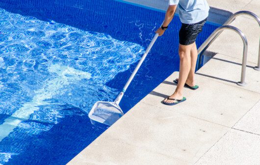 Foto que ilustra matéria sobre como limpar piscina mostra um homem limpando a piscina de casa
