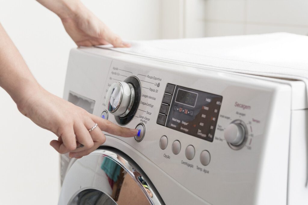 Foto que ilustra matéria sobre como limpar máquina de lavar mostra uma mulher ligando uma máquina de lavar.