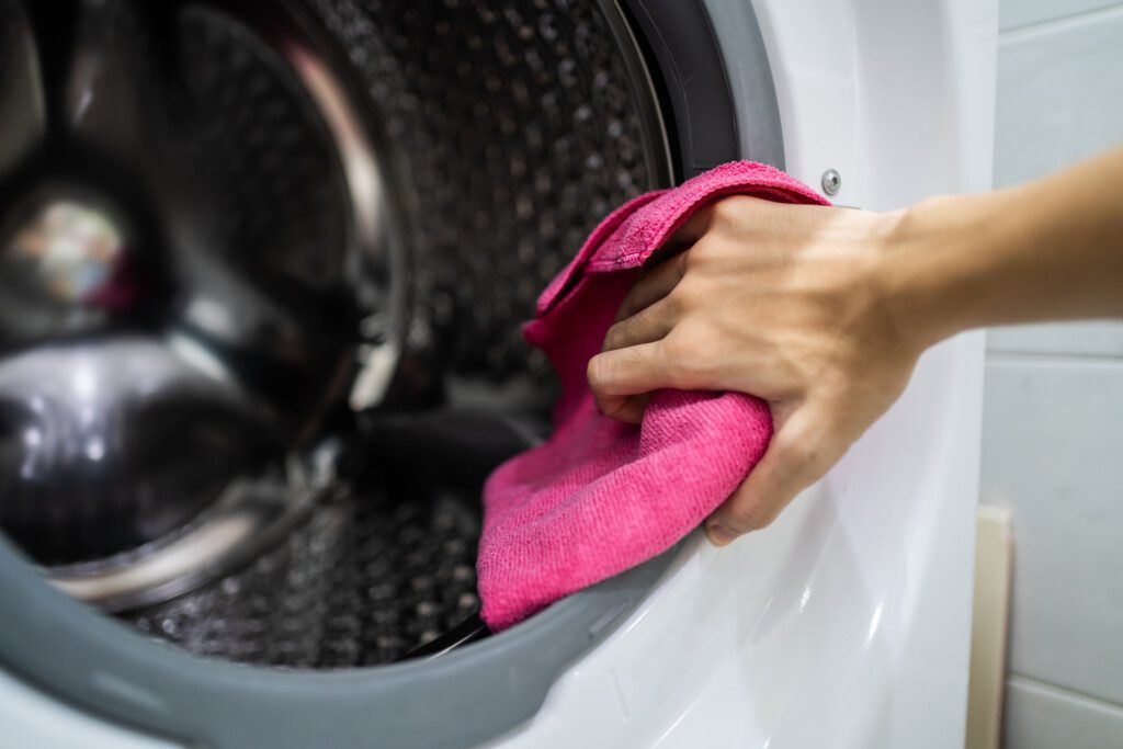 Foto que ilustra matéria sobre como limpar máquina de lavar mostra uma pessoa limpando uma máquina de lavar com pano seco