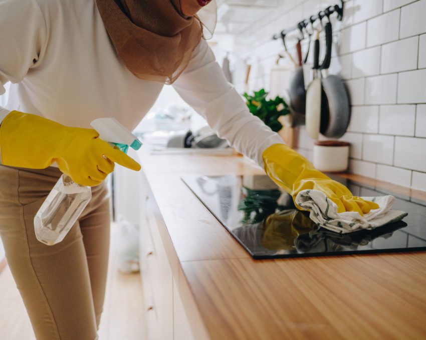 Imagem de uma mulher com luvas de borracha limpando um fogão de vidro com pano.