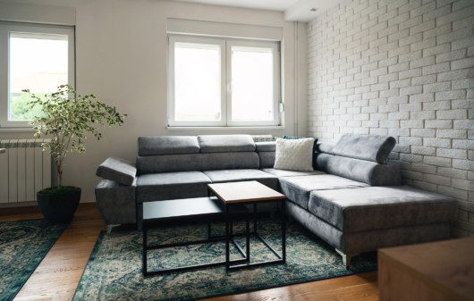 Imagem de uma sala de estar cinza com detalhes em preto e uma parede branca de tijolinhos.