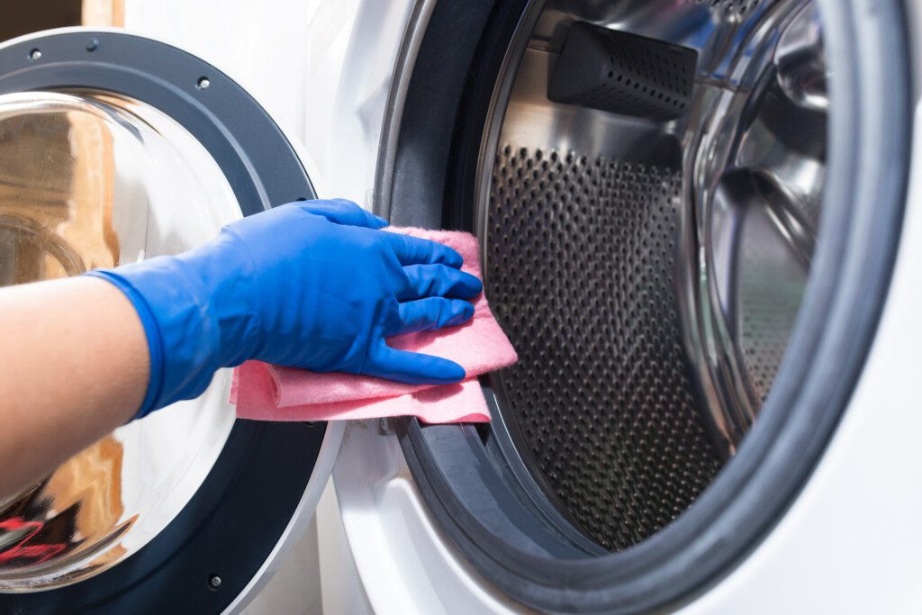 Foto que ilustra matéria sobre como limpar máquina de lavar mostra uma pessoa limpando uma máquina de lavar com luvas