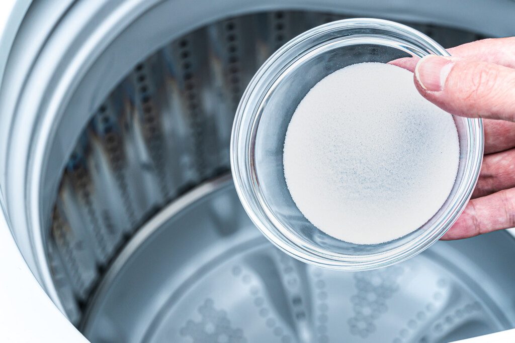 Foto que ilustra matéria sobre como limpar máquina de lavar mostra uma pessoa segurando uma xícara de bicarbonato de sódio para adicionar na máquina de lavar