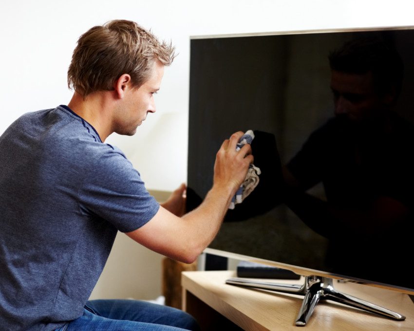 Imagem de um homem limpando a tela de uma TV com uma flanela.