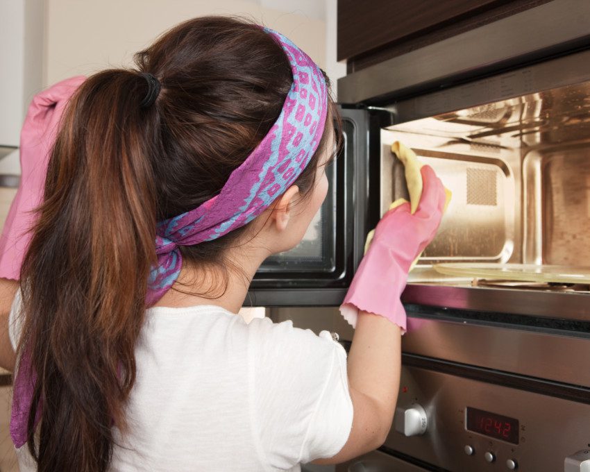Imagem de uma mulher limpando microondas por dentro com luvas de proteção.