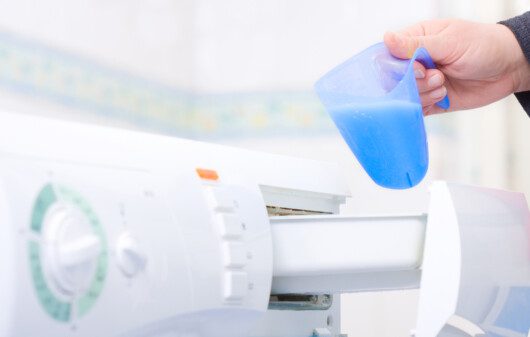 Foto que ilustra matéria sobre como limpar máquina de lavar mostra uma pessoa colocando sabão na máquina