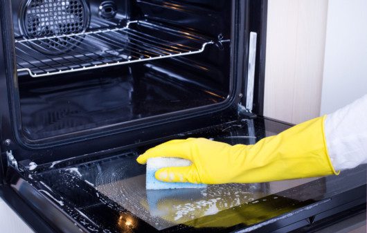 Imagem de uma pessoa limpando um forno elétrico com esponja e detergente.