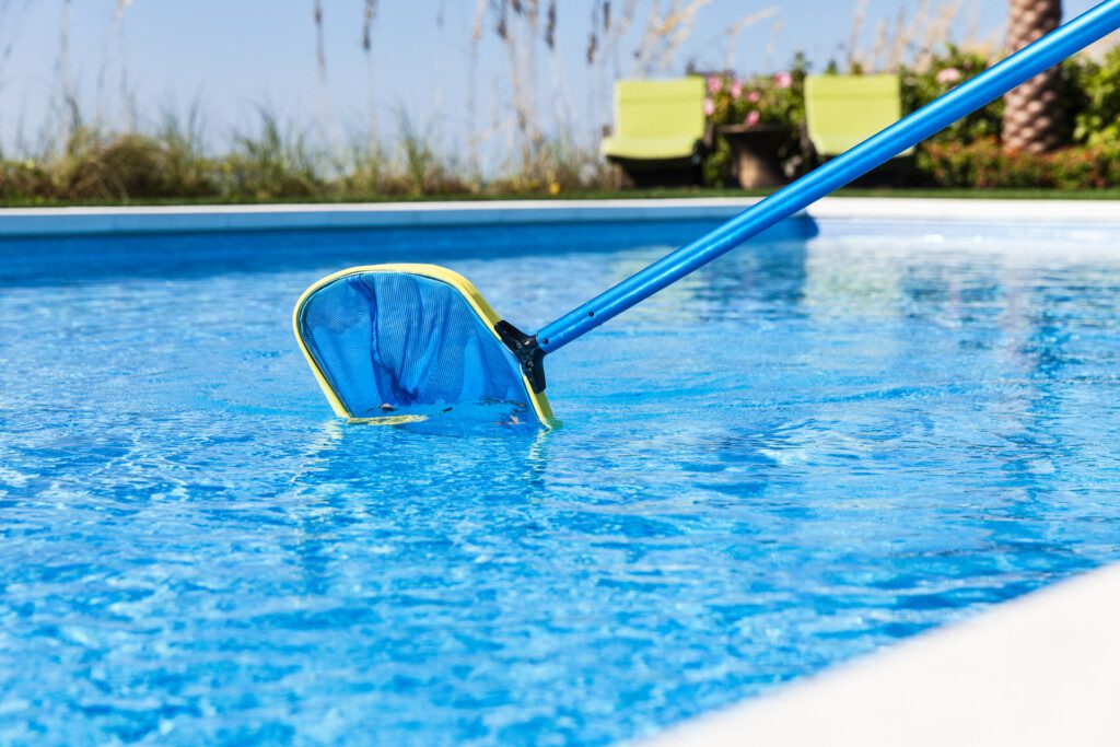 Foto que ilustra matéria sobre como limpar piscina mostra uma pessoas segurando uma peneira em uma piscina