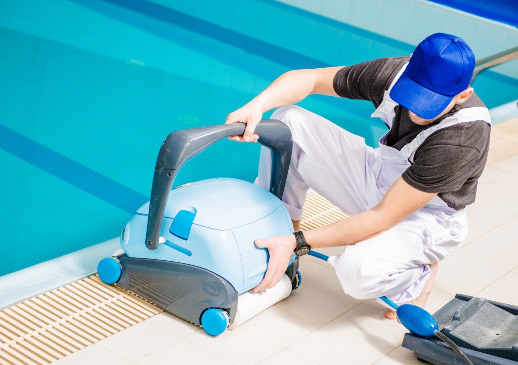 Foto que ilustra matéria sobre como limpar piscina mostra um homem ligando o aspirador de pó de uma piscina.