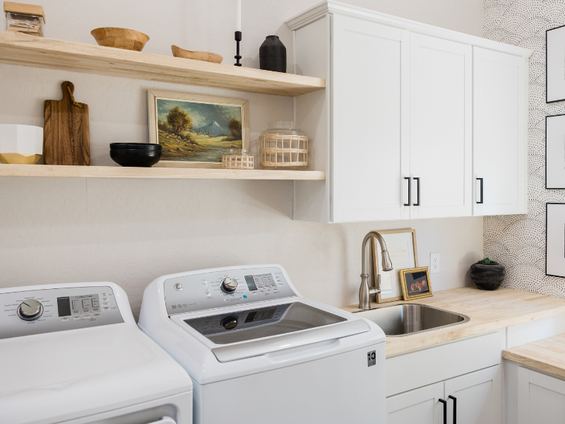 Imagem mostra lavanderia, com das máquinas de lavar, pia e armários suspensos. Foto disponível no Canva